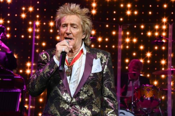 Rod Stewart singing into a microphone on stage while wearing a floral shiny blazer