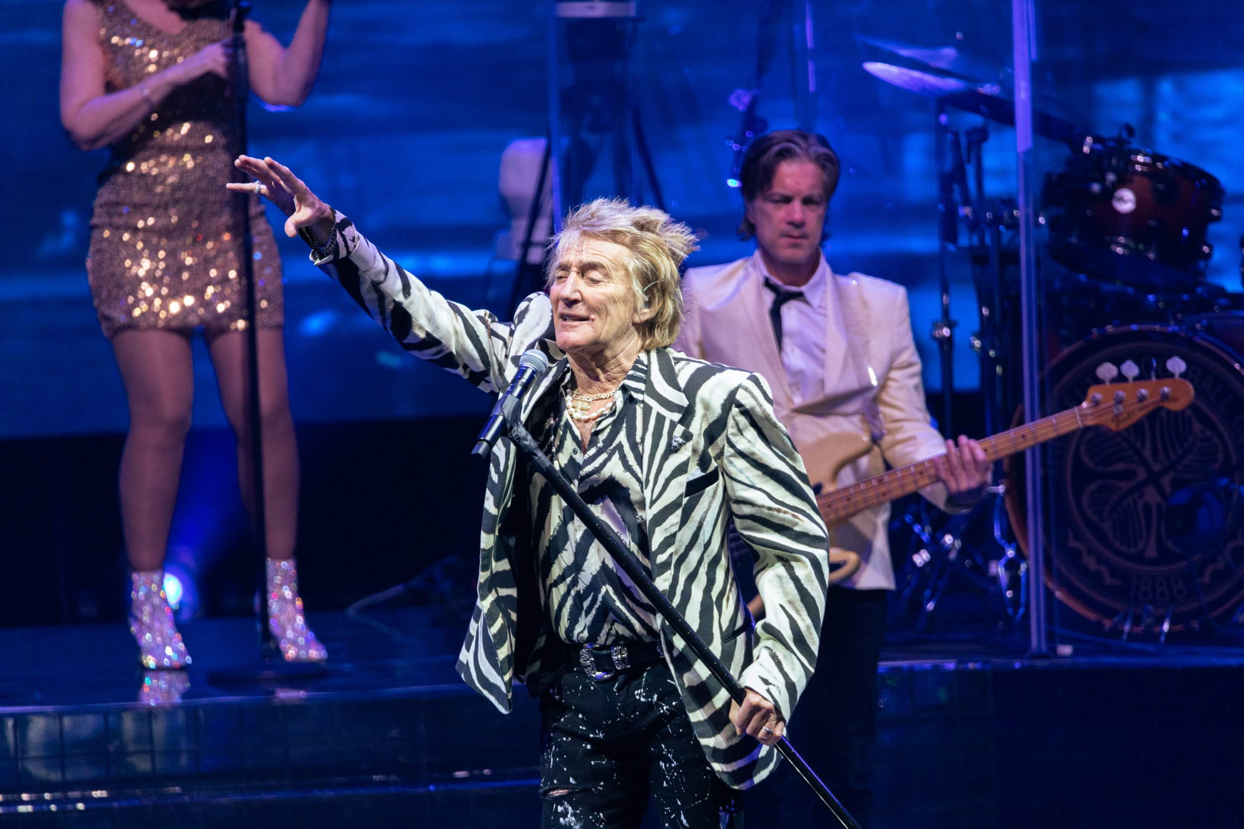 Sir Rod Stewart singing into a microphone while wearing a zebra print blazer