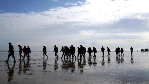 People walking across after alighting a boat which can be seen in the background